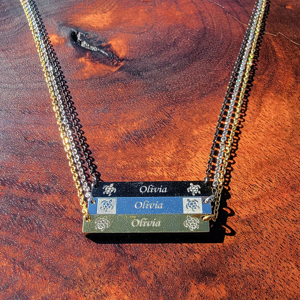 Stainless steel horizontal bar pendants engraved with honu designs on each side of a personalized message